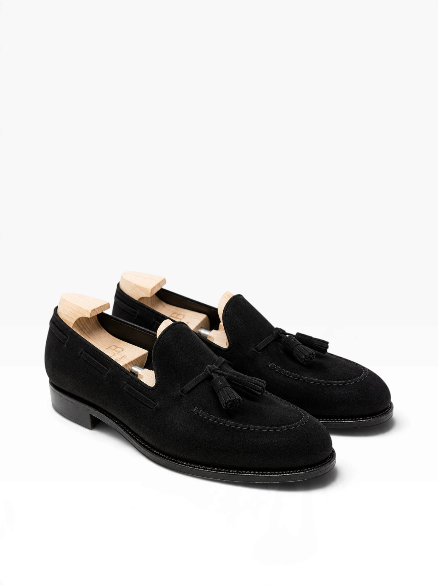 Bourgee a world class shoe store black suede tassel loafers with wooden shoe trees on a white background