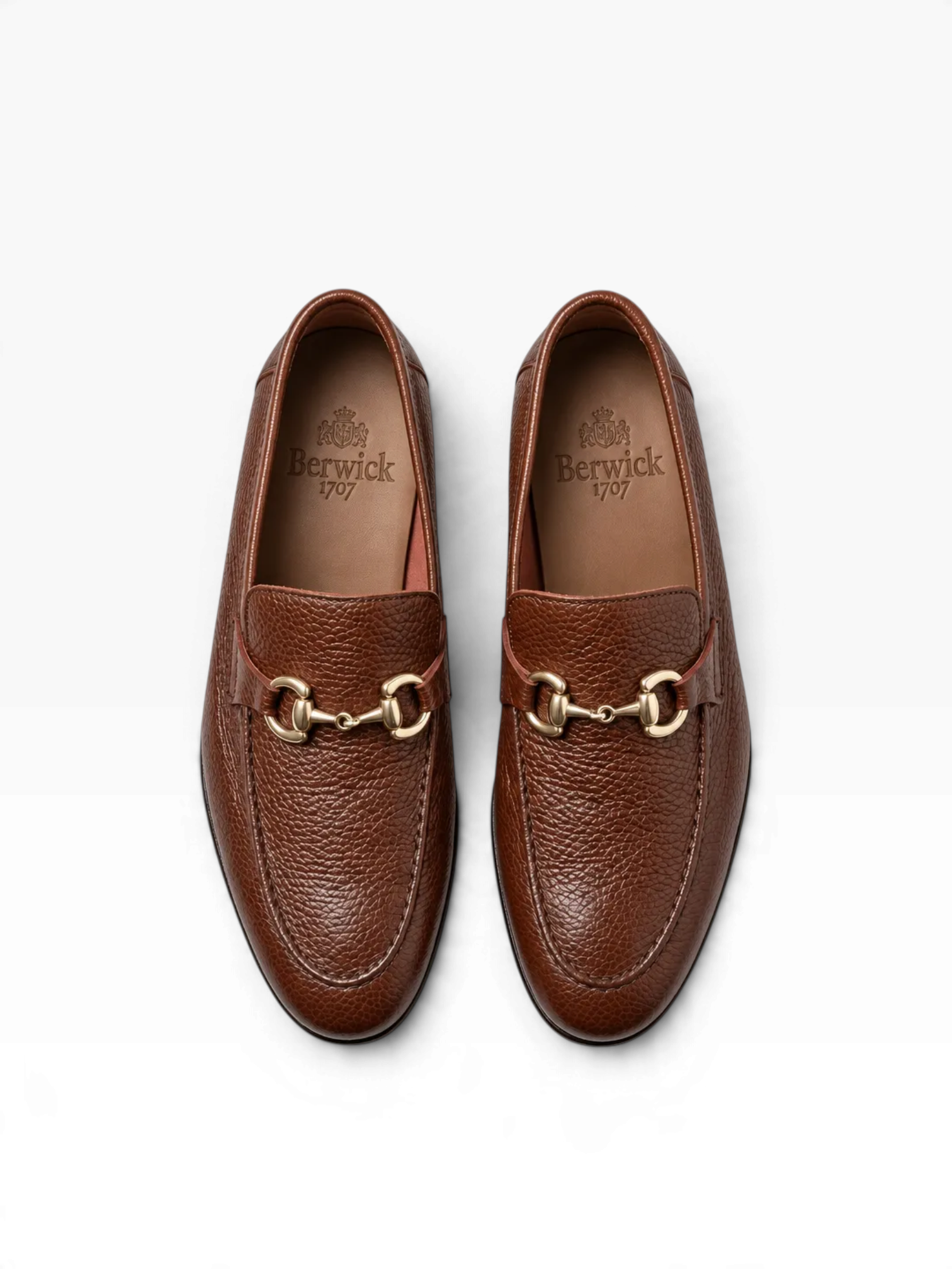 A pair of brown pebbled leather penny loafers with gold-tone horsebit hardware, shown from a top-down view on a white background. The brand name 'Berrick' is visible on the insoles.