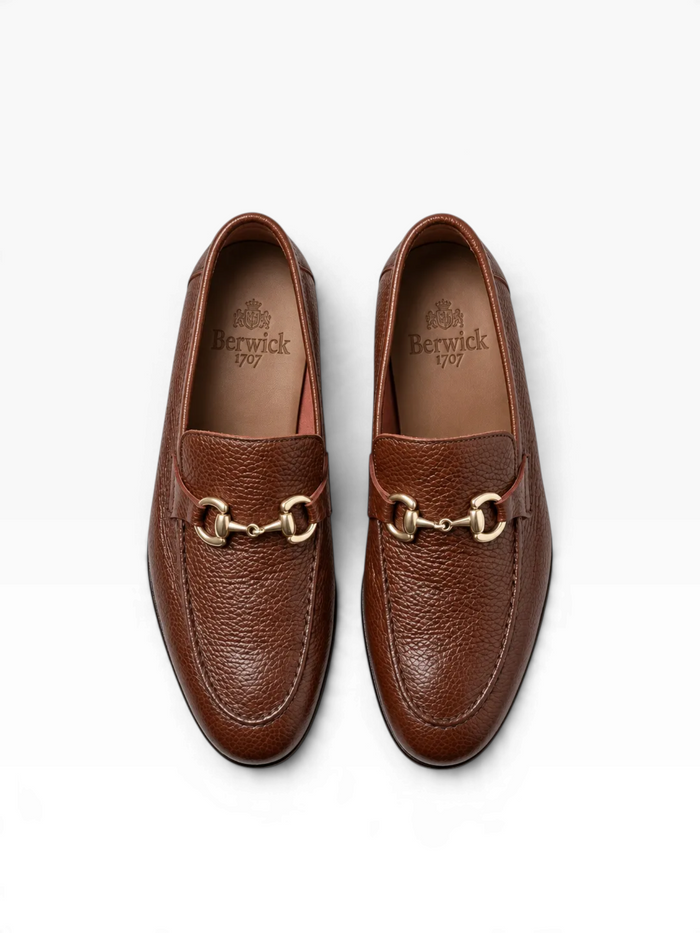 A pair of brown pebbled leather penny loafers with gold-tone horsebit hardware, shown from a top-down view on a white background. The brand name 'Berrick' is visible on the insoles.